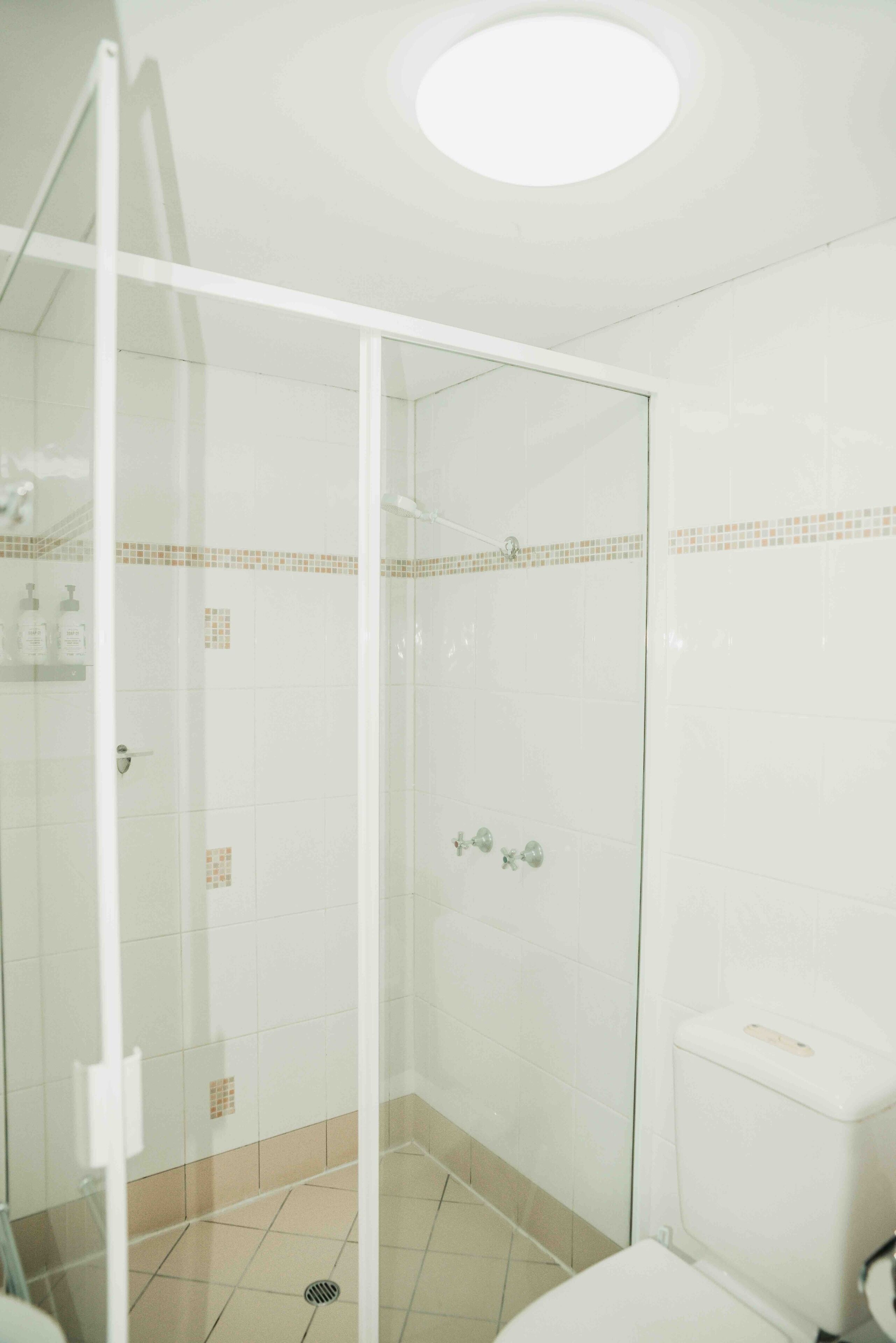 A bathroom with a glass-enclosed shower, a toilet, and a sink.