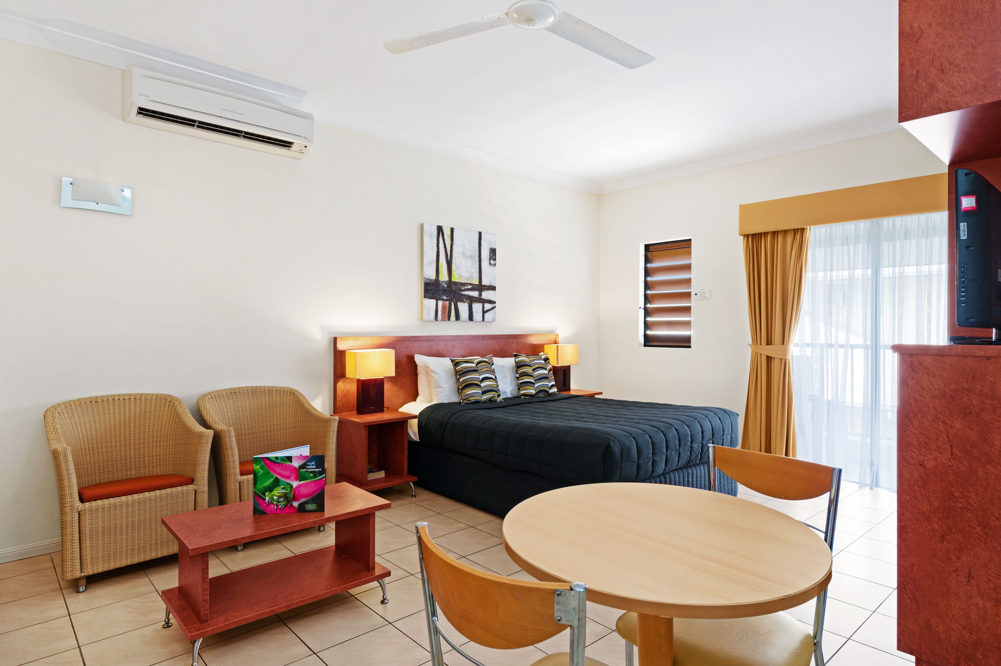 Een hotelkamer met een bed, twee stoelen, een tafel, een televisie en een airconditioner.
