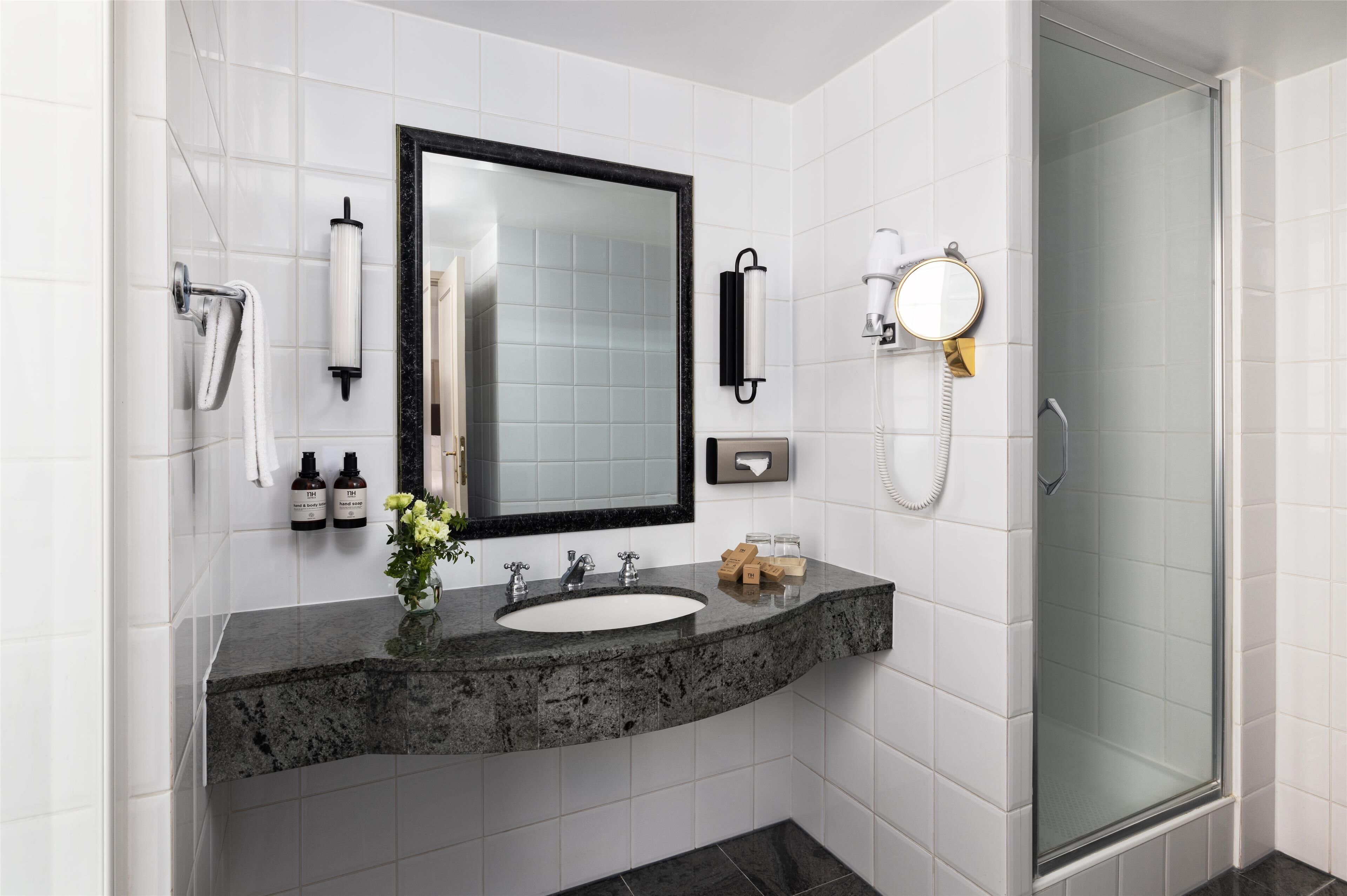 A modern bathroom with a marble sink, a large mirror, a glass-enclosed shower, and toiletries on the wall.
