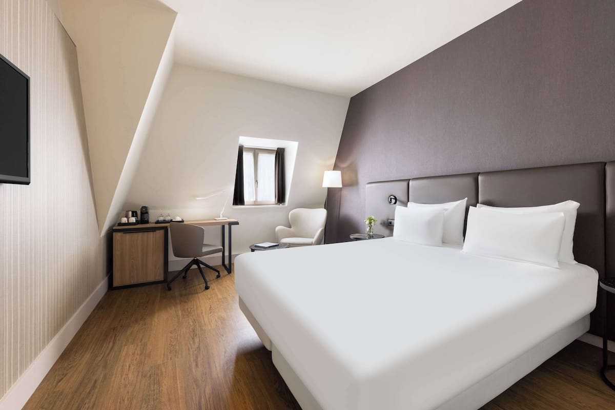 Une chambre d’hôtel moderne équipée d’un grand lit, d’un bureau, d’une chaise et d’une petite table.