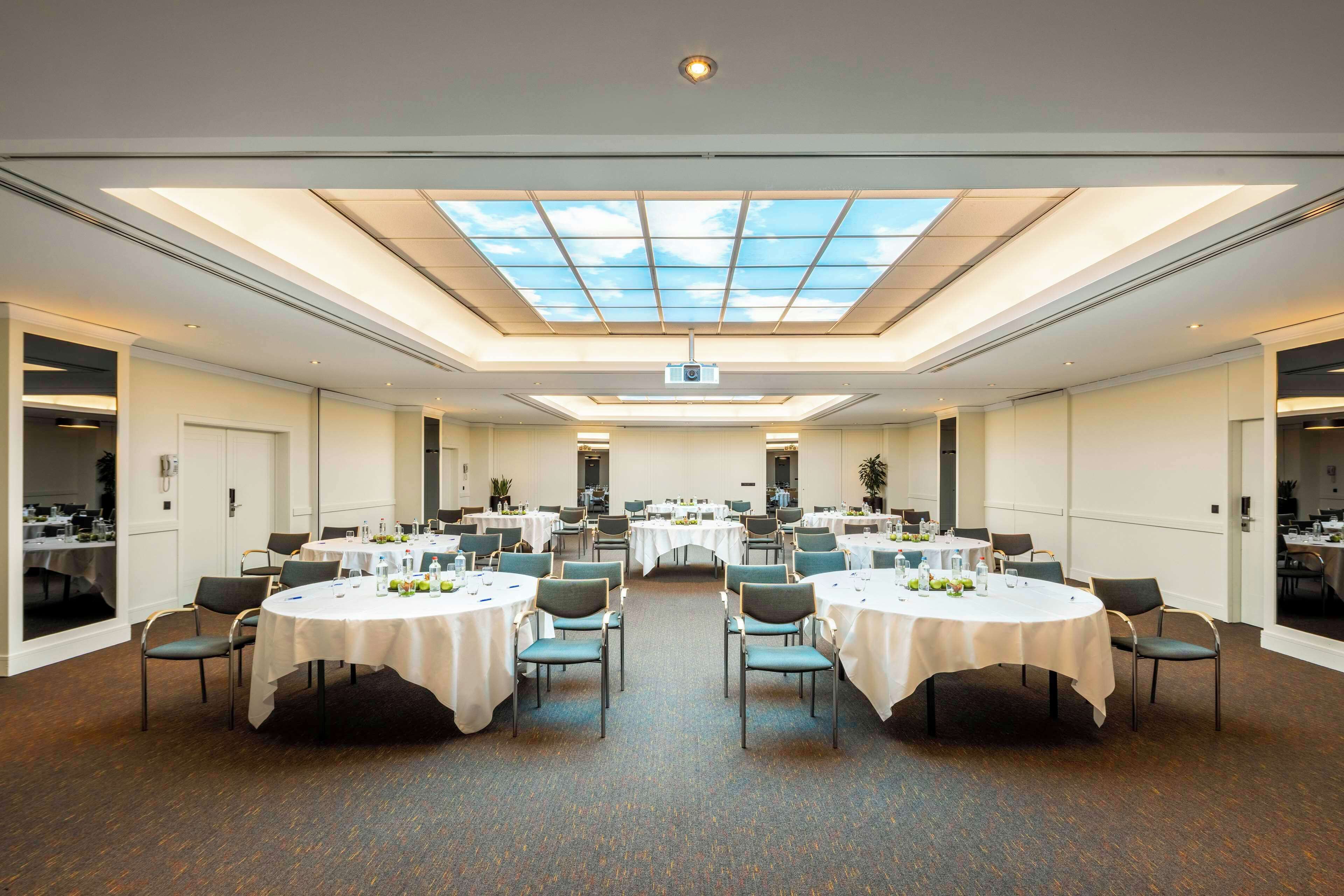 A conference room with round tables, chairs, and a skylight ceiling.