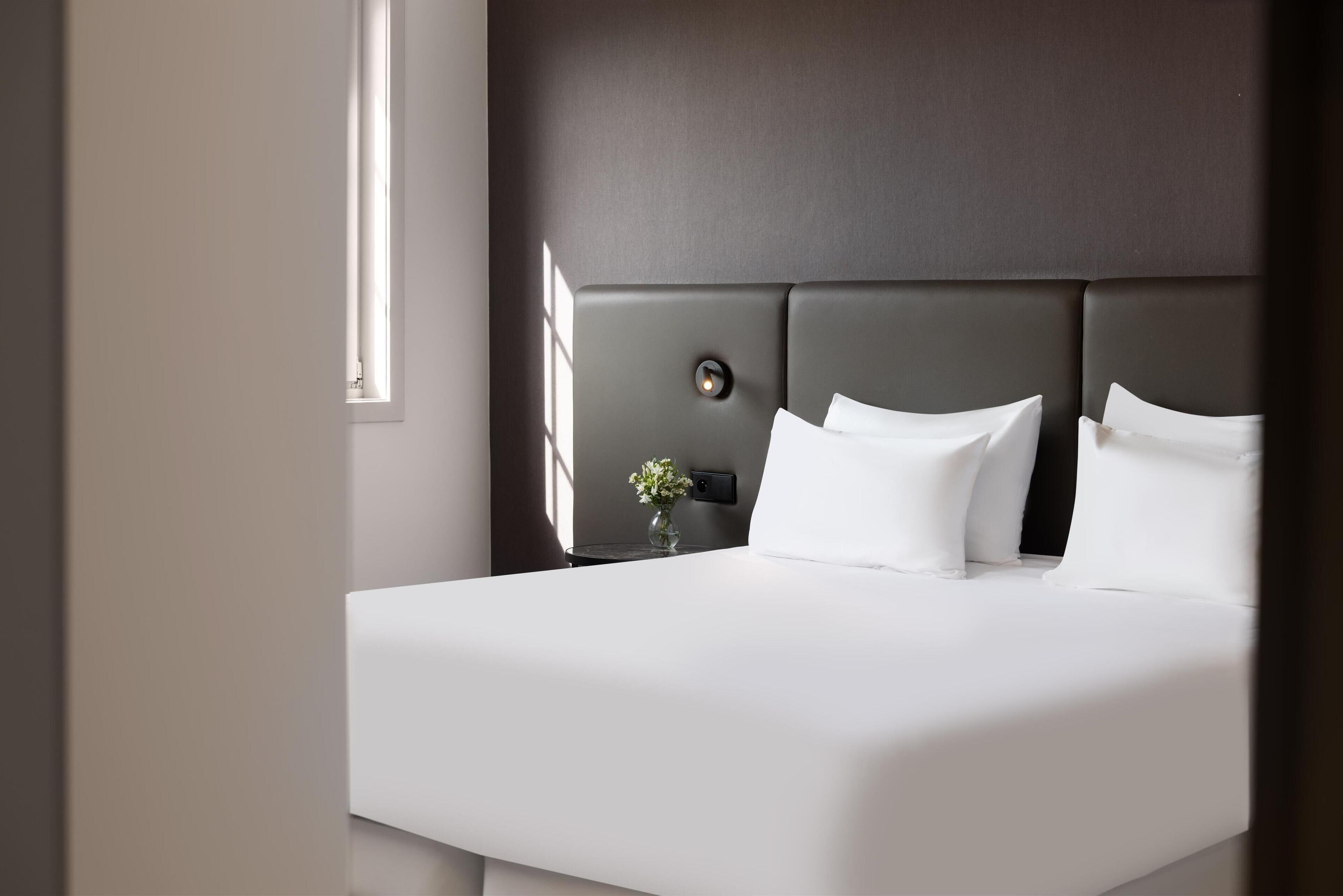 Una habitación de hotel moderna con una cama grande, una mesita de noche y un pequeño florero con flores.
