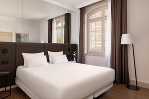 Une chambre d’hôtel moderne avec un grand lit, une table de chevet, une lampe sur pied et une fenêtre avec des rideaux.