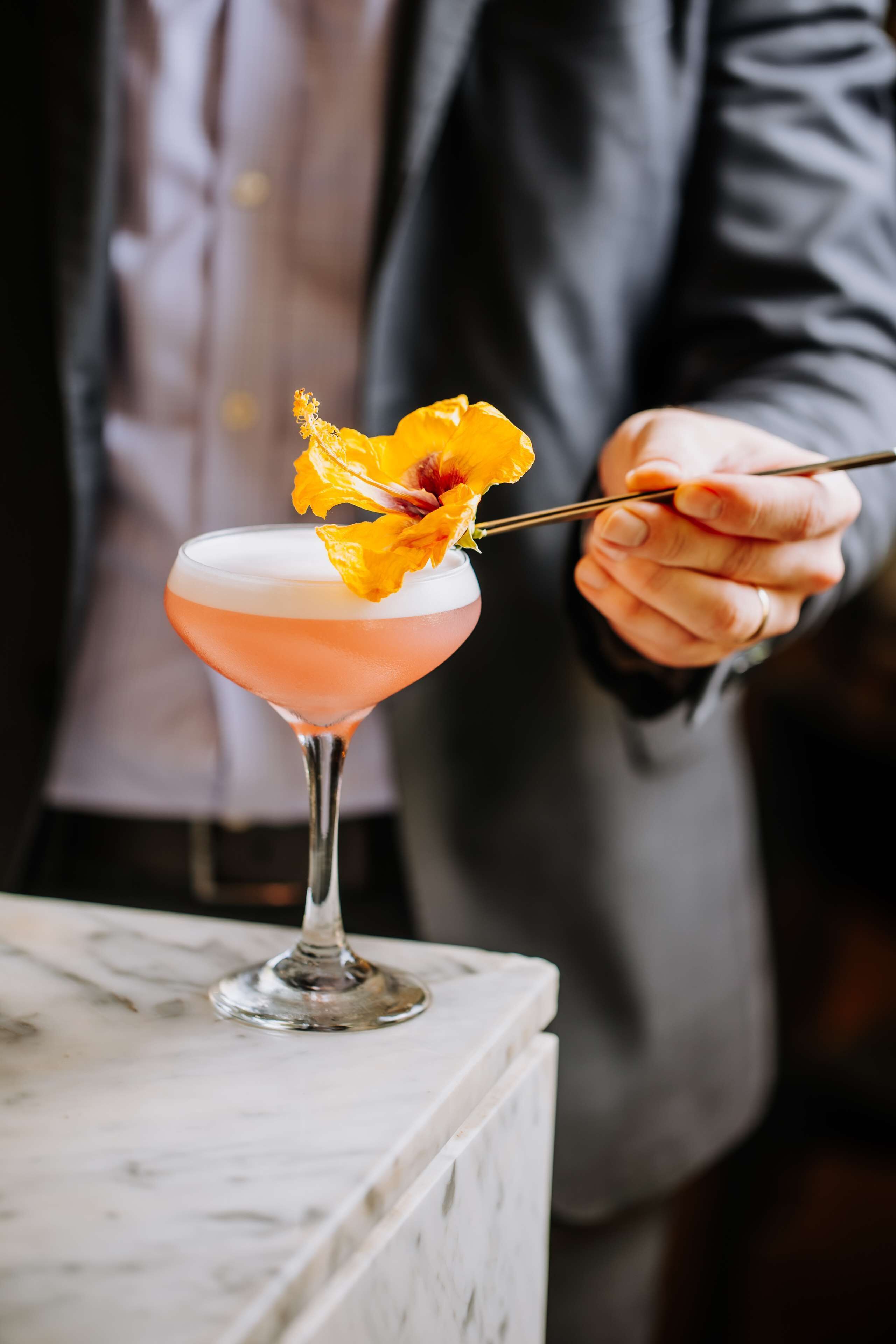 A cocktail with a flower garnish on a marble bar counter.