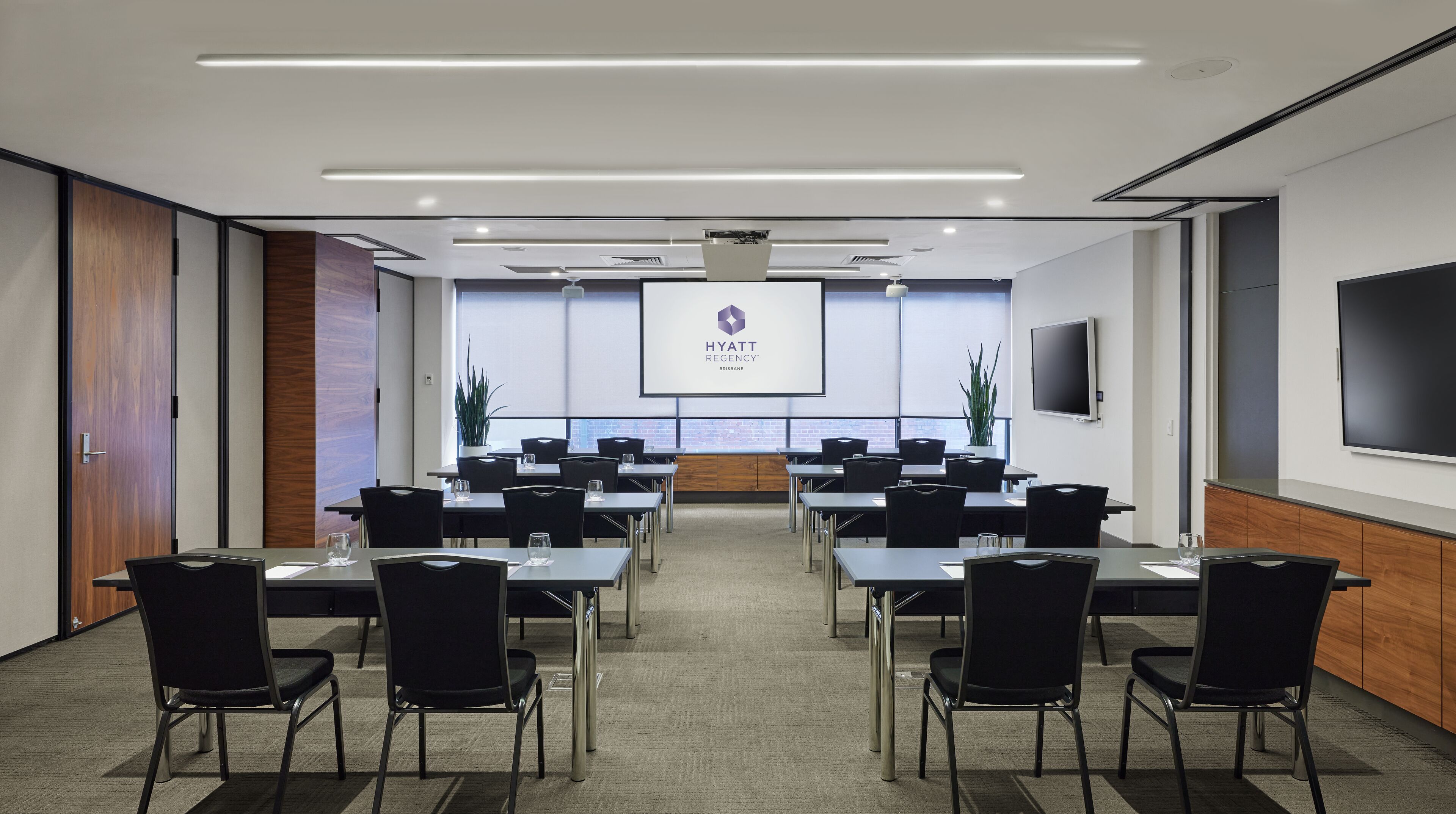 Une salle de conférence dotée d’un grand écran affichant le logo du Hyatt Regency Brisbane, de plusieurs tables avec des chaises et d’un grand téléviseur à écran plat fixé au mur.