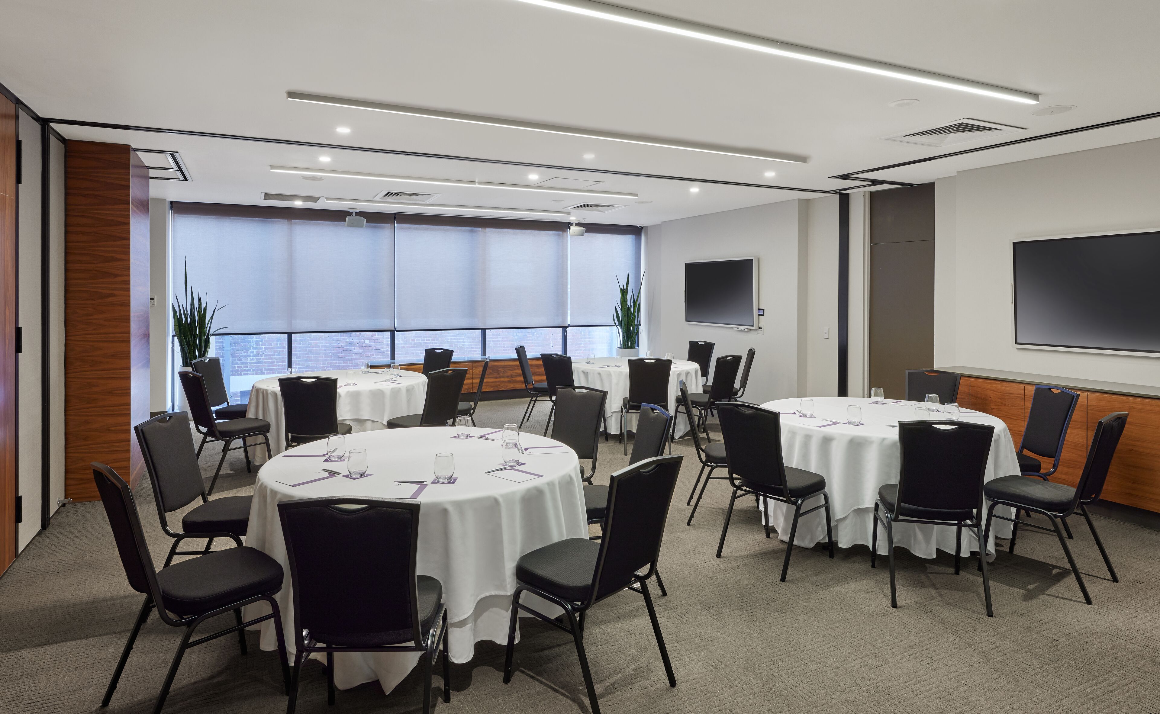 A conference room with round tables, black chairs, and a large screen on the wall.