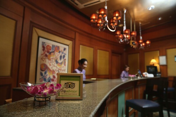 A reception area with a glass bowl of fruit, a framed TripAdvisor sign, and a chandelier.
