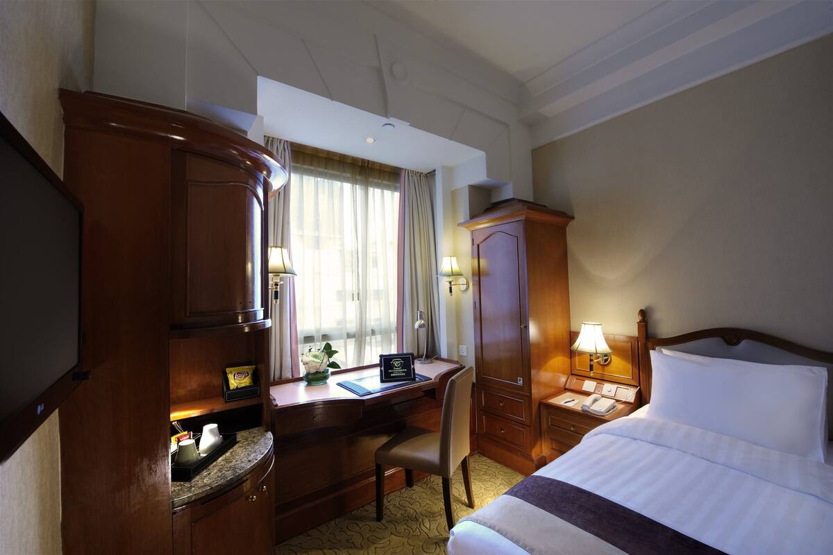 Quarto de hotel com uma cama, uma mesa com um computador, uma cadeira, um telefone e um abajur.