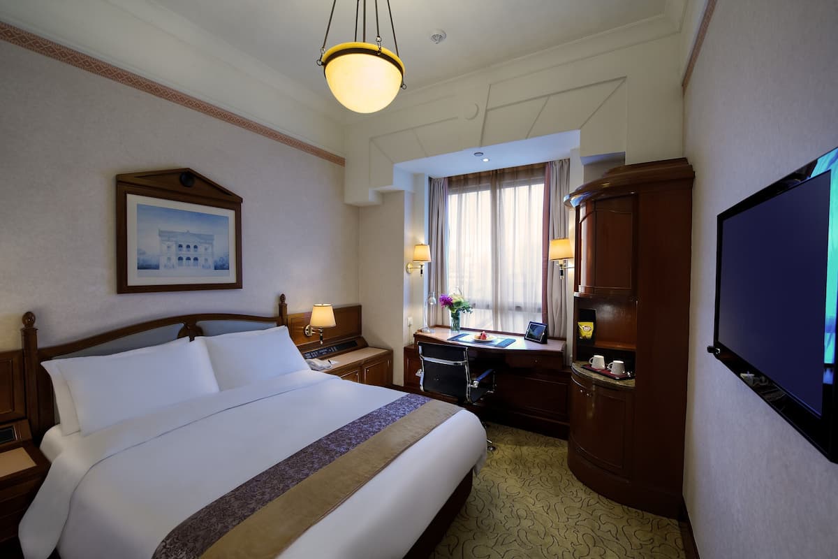 Quarto de hotel com uma cama grande, uma escrivaninha com computador, televisão e janela com cortinas.