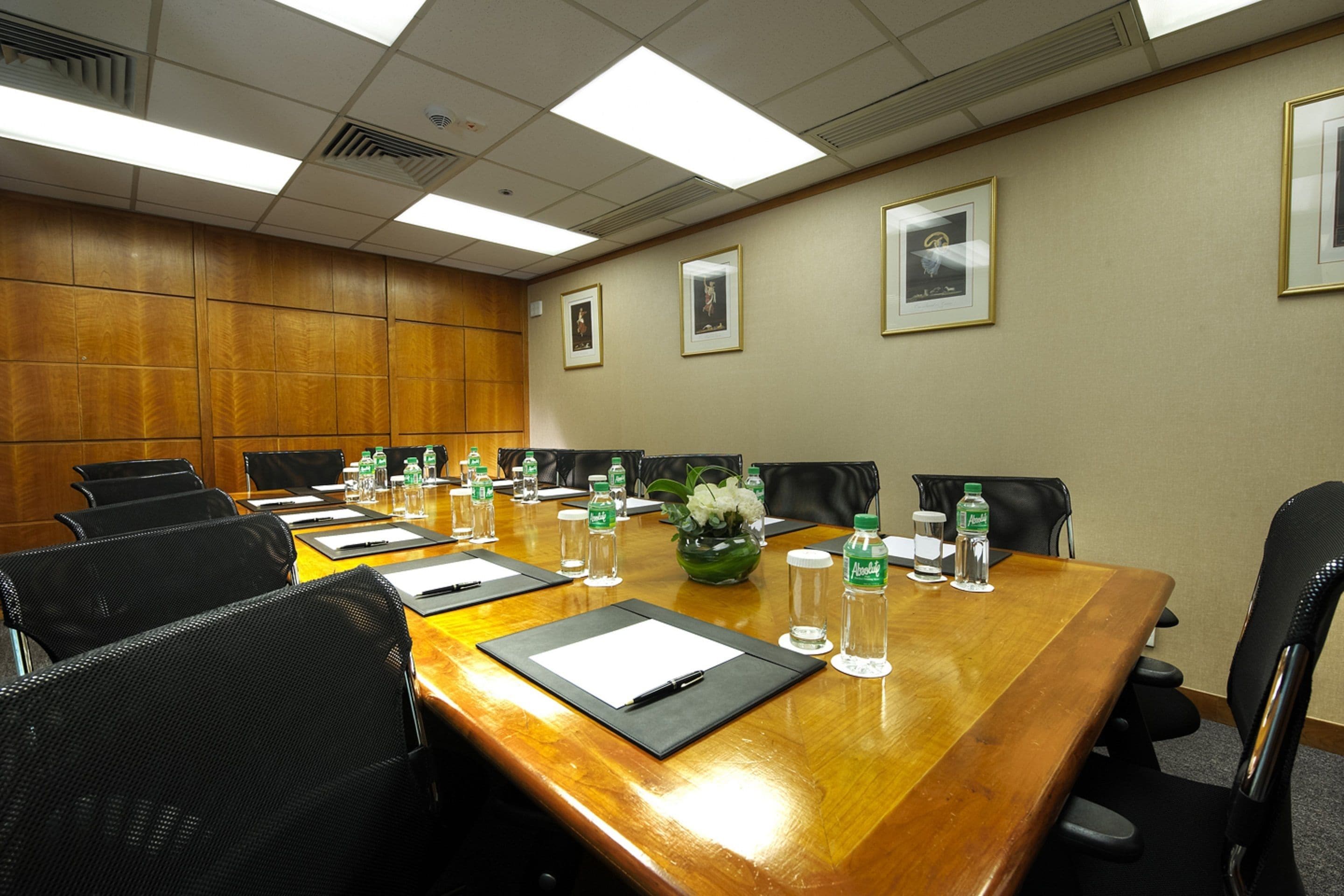 A conference room with a long wooden table, black chairs, and framed pictures on the wall.