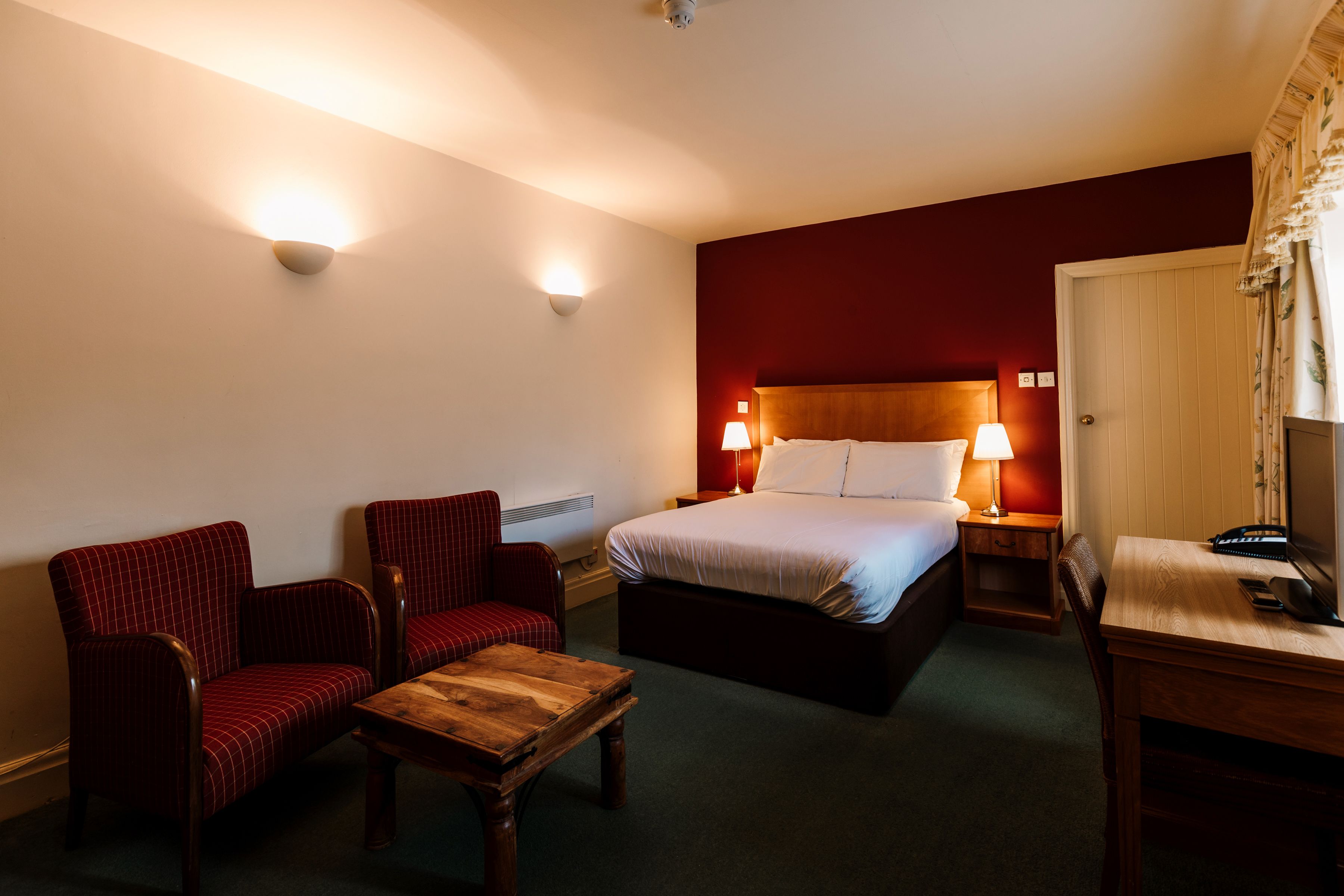 A hotel room with a bed, two armchairs, a wooden table, and a desk with a telephone.