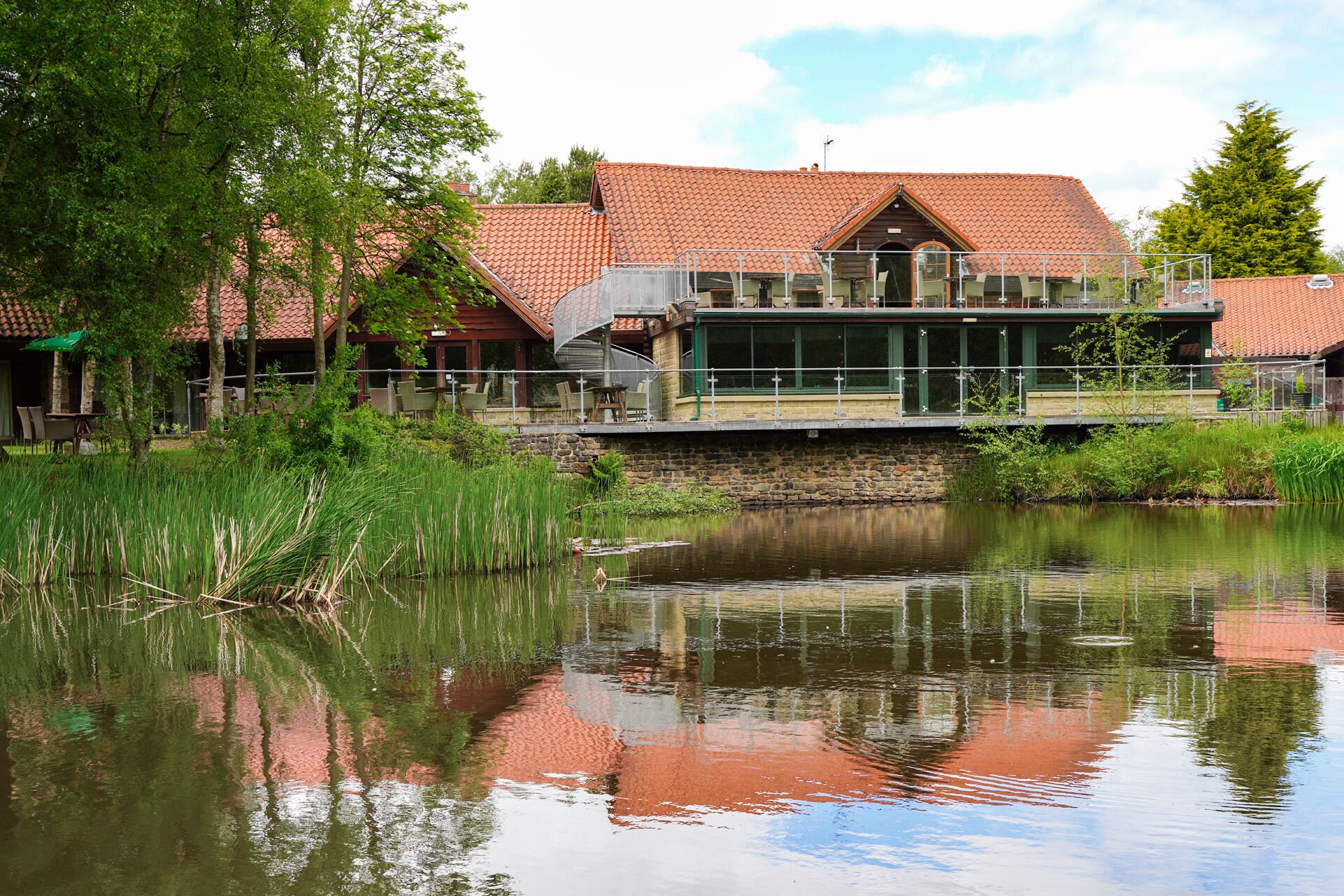 Een hotel aan het meer, met een stenen gevel, een glazen conservatorium en een houten terras met uitzicht op het water.