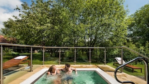 A swimming pool with a metal railing, surrounded by trees and a bench.