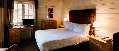 Ein Hotelzimmer mit Bett, Schreibtisch mit Fernseher, Stuhl, Nachttisch mit Lampe und Telefon.