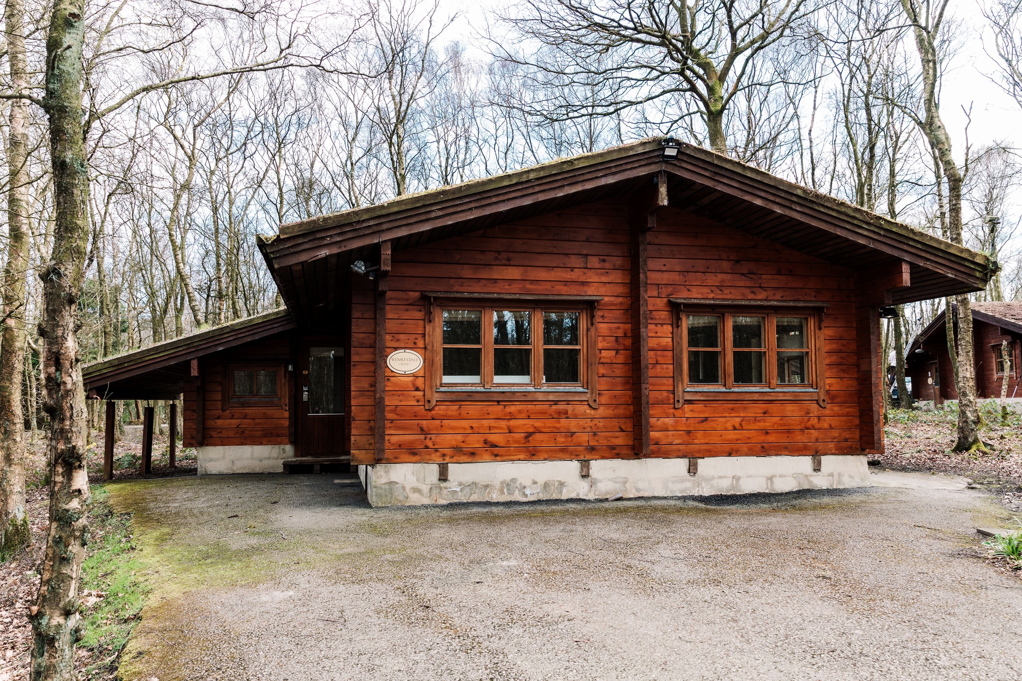 A wooden cabin with a sloped roof, large windows, and a gravel driveway.