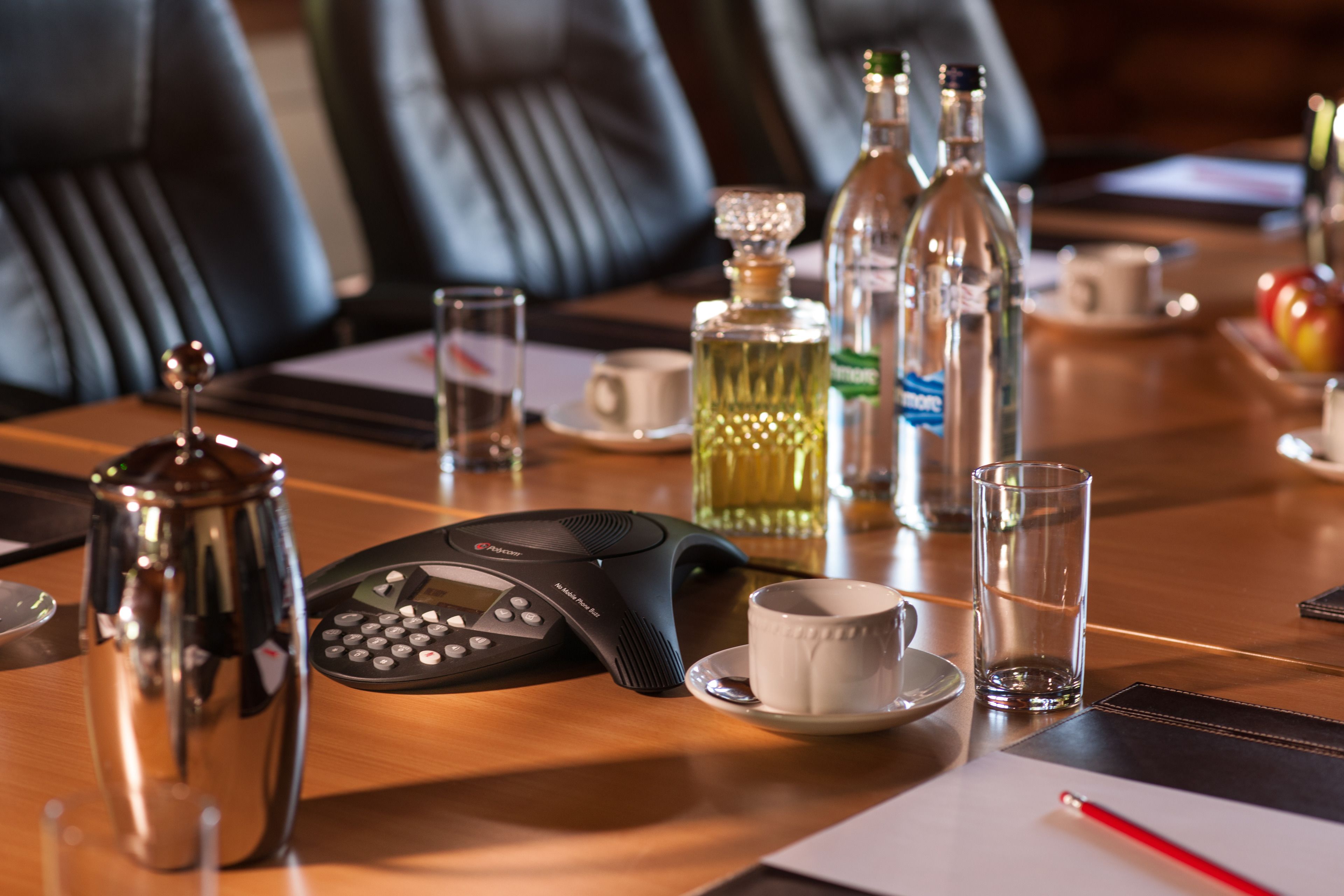 A conference table with a telephone, a coffee pot, a glass, a bottle, and a cup.