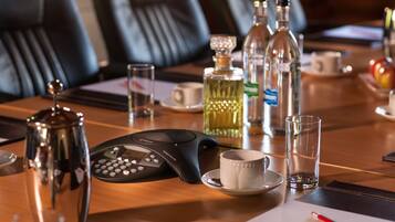 A conference table with a telephone, a coffee pot, a glass, a bottle, and a cup.