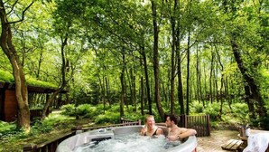 A hot tub surrounded by a wooden deck and lush greenery in a forested area.