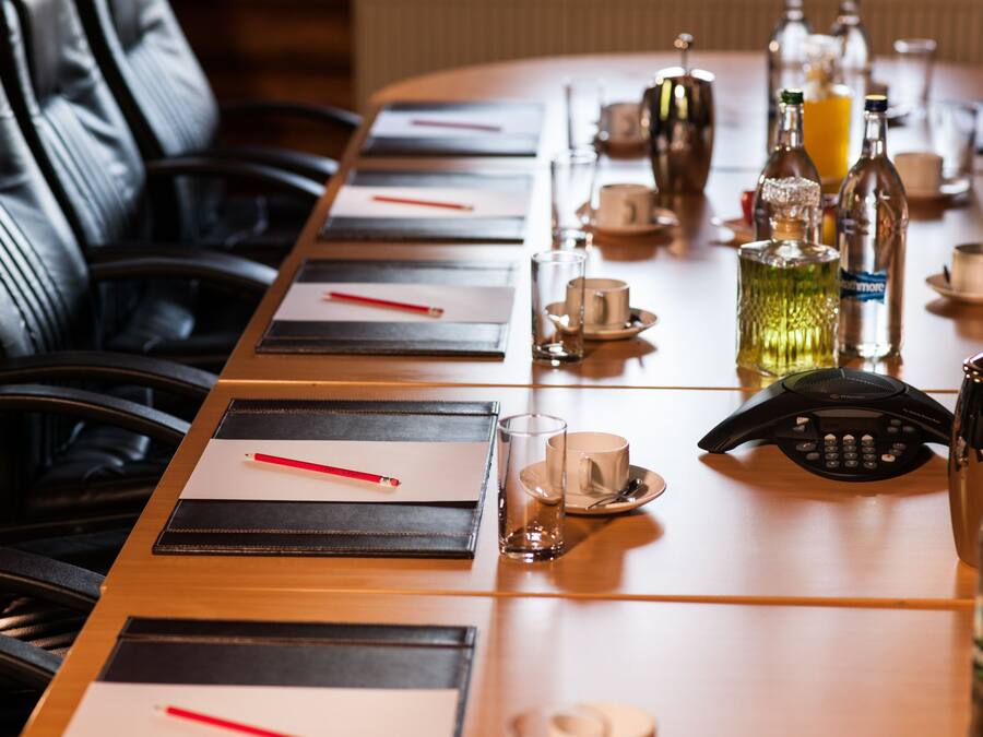 A conference table with black placemats, red pencils, and clear glasses.