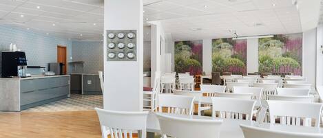 A modern hotel lobby with a reception area, a large mural of flowers, and rows of white chairs.