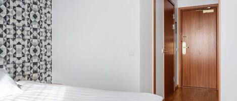 A bedroom with a bed, a geometric-patterned wall, and a wooden door.