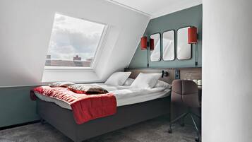 Un dormitorio con cama, escritorio, silla, ventana y espejo fijado a la pared.