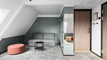 A modern room with a grey sofa, a red ottoman, a small table, a wardrobe, and a door with a mirror.