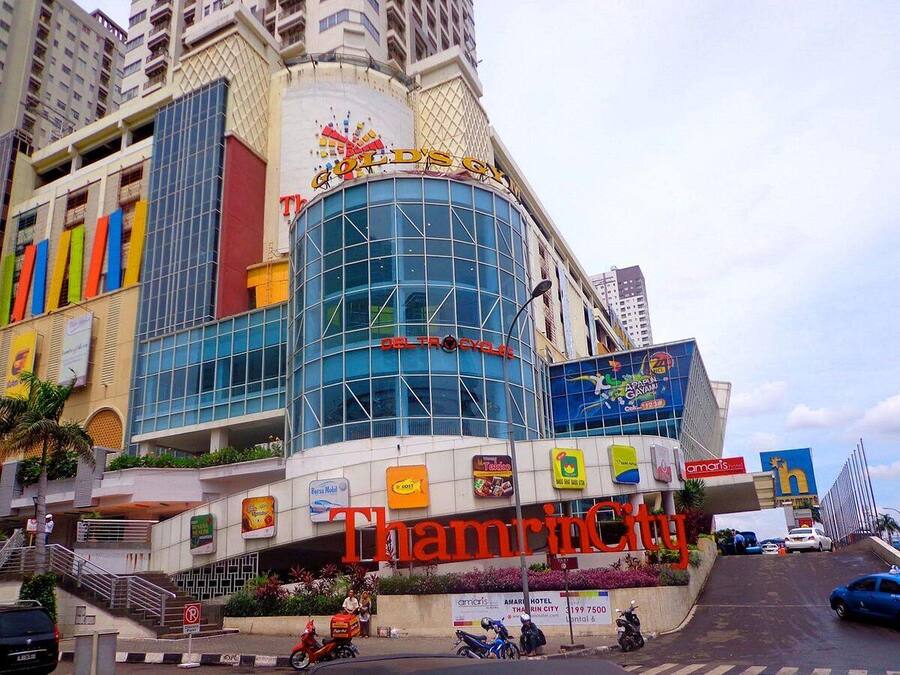 A multi-story building with a prominent 'Thamrin City' sign, various commercial signs, and a mix of modern and traditional architecture.