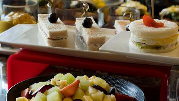 En buffet med forskellige retter, herunder sandwiches og en frugtsalat.