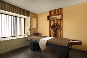 Ein moderner Spa-Bereich mit einer Massageliege, einem großen Fenster mit vertikalen Jalousien, einem Waschbecken und einem Regal mit Dekoration.