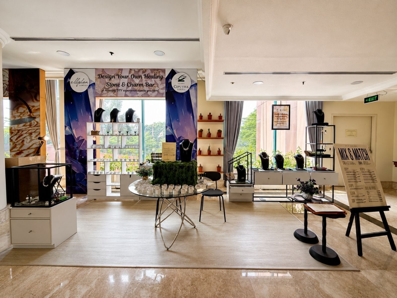 L’intérieur d’une bijouterie, avec un comptoir où sont exposés des pierres et des breloques, des tables de présentation où sont disposés des bijoux, et un panneau affichant les prix.