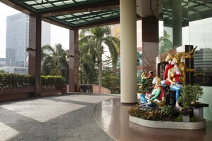 A spacious lobby with a central sculpture, large pillars, and a view of a tall building in the background.