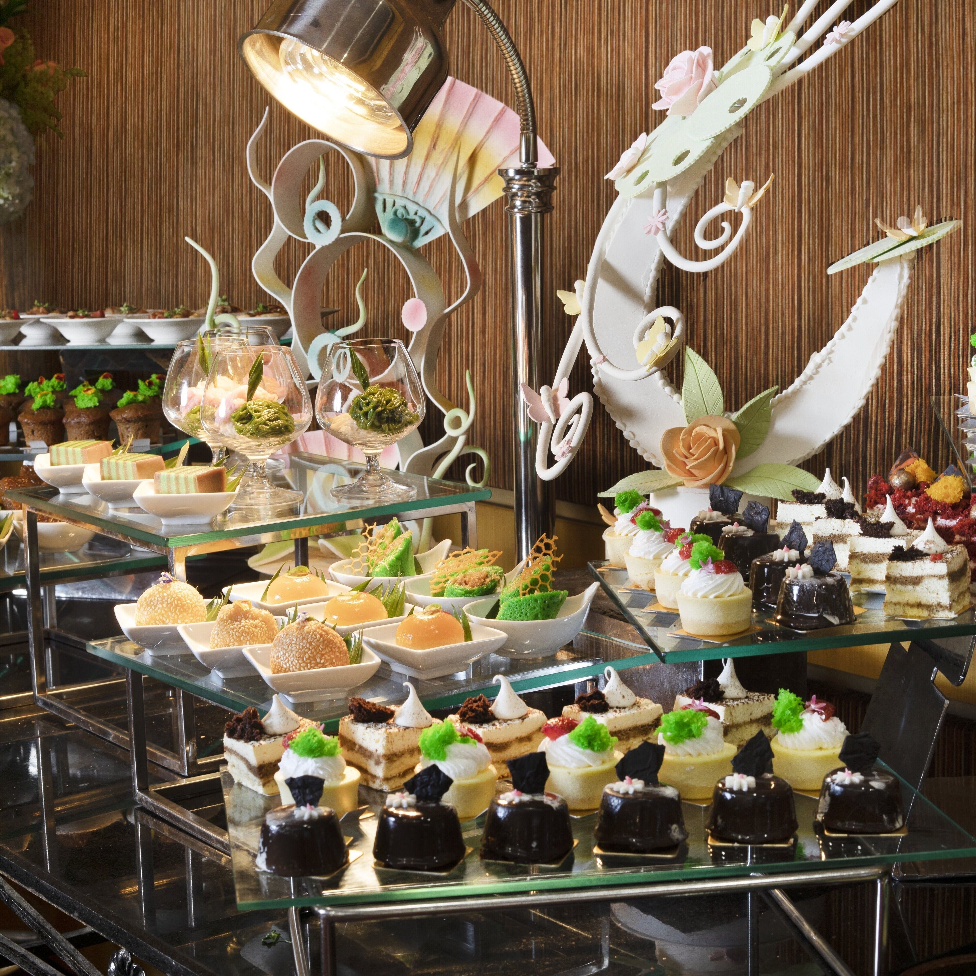 Un buffet con diversi dolci e pasticcini, tra cui torte e crostate di frutta, esposti su scaffali di vetro.