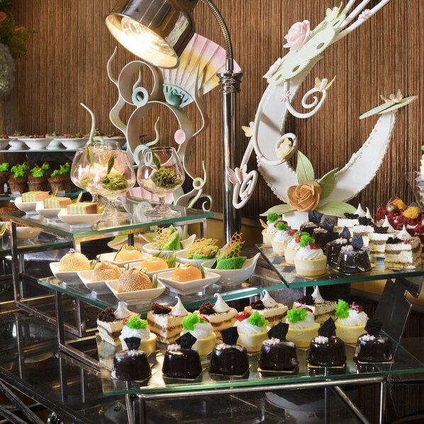 Un bufé con diversos postres y pasteles, incluyendo tartas de pastel y tartaletas de fruta, exhibidos en estantes de vidrio.
