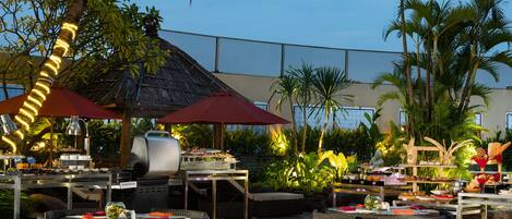 An outdoor dining area with wicker furniture, a grill, and a view of the ocean.