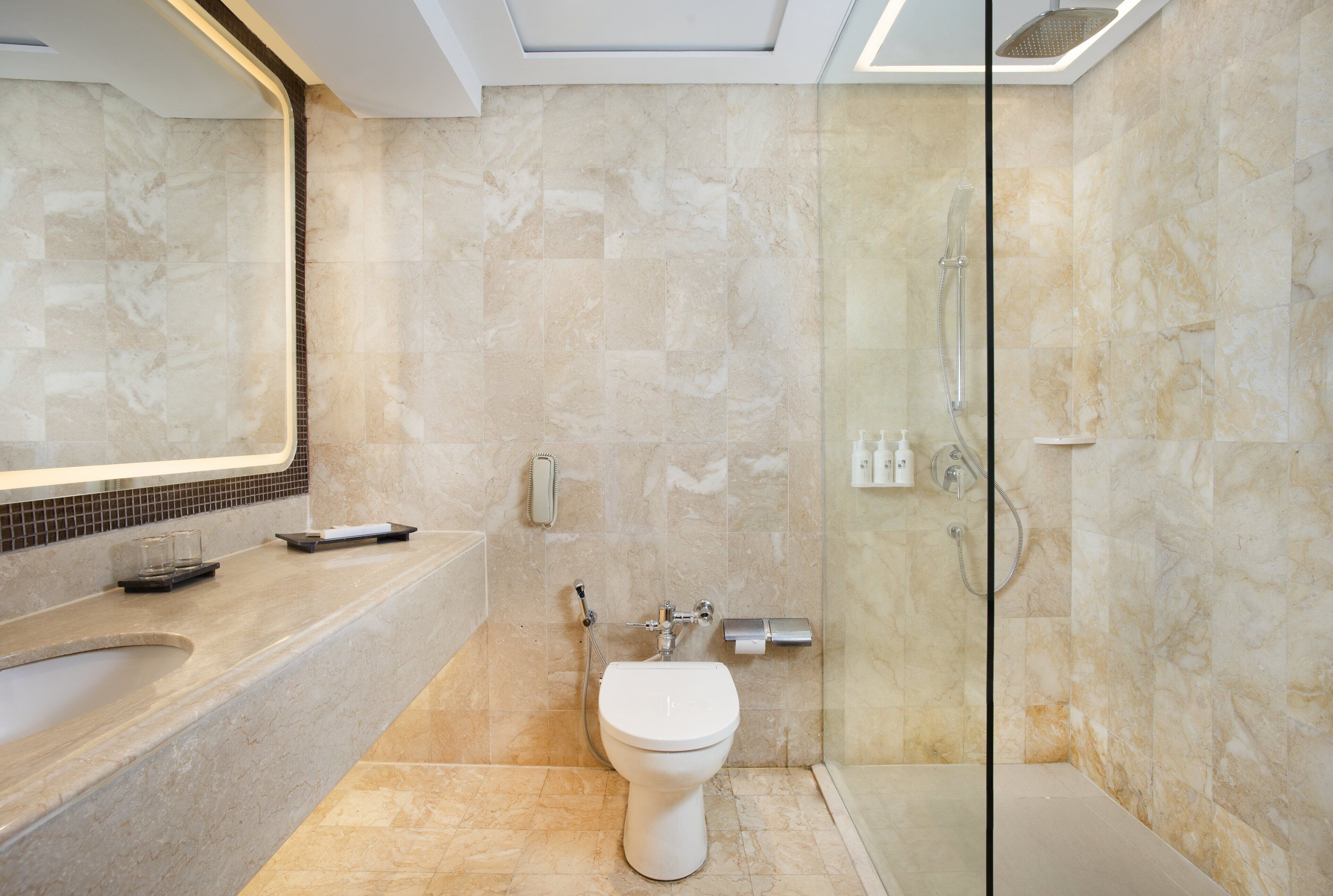 Une salle de bain moderne avec un lavabo en marbre, des toilettes et une douche séparée par une paroi de verre.