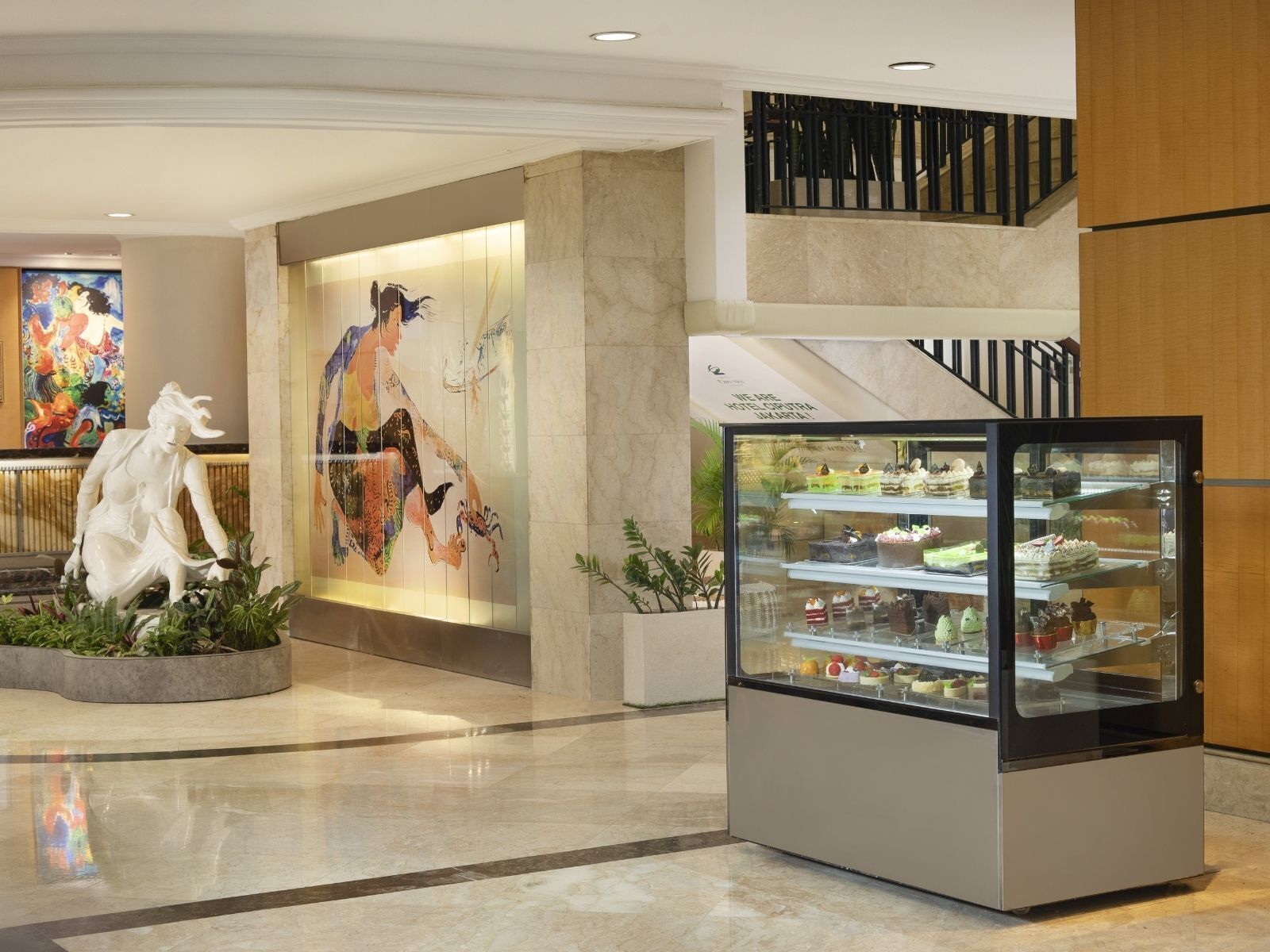 A lobby with a sculpture, a mural, a staircase, and a dessert display.