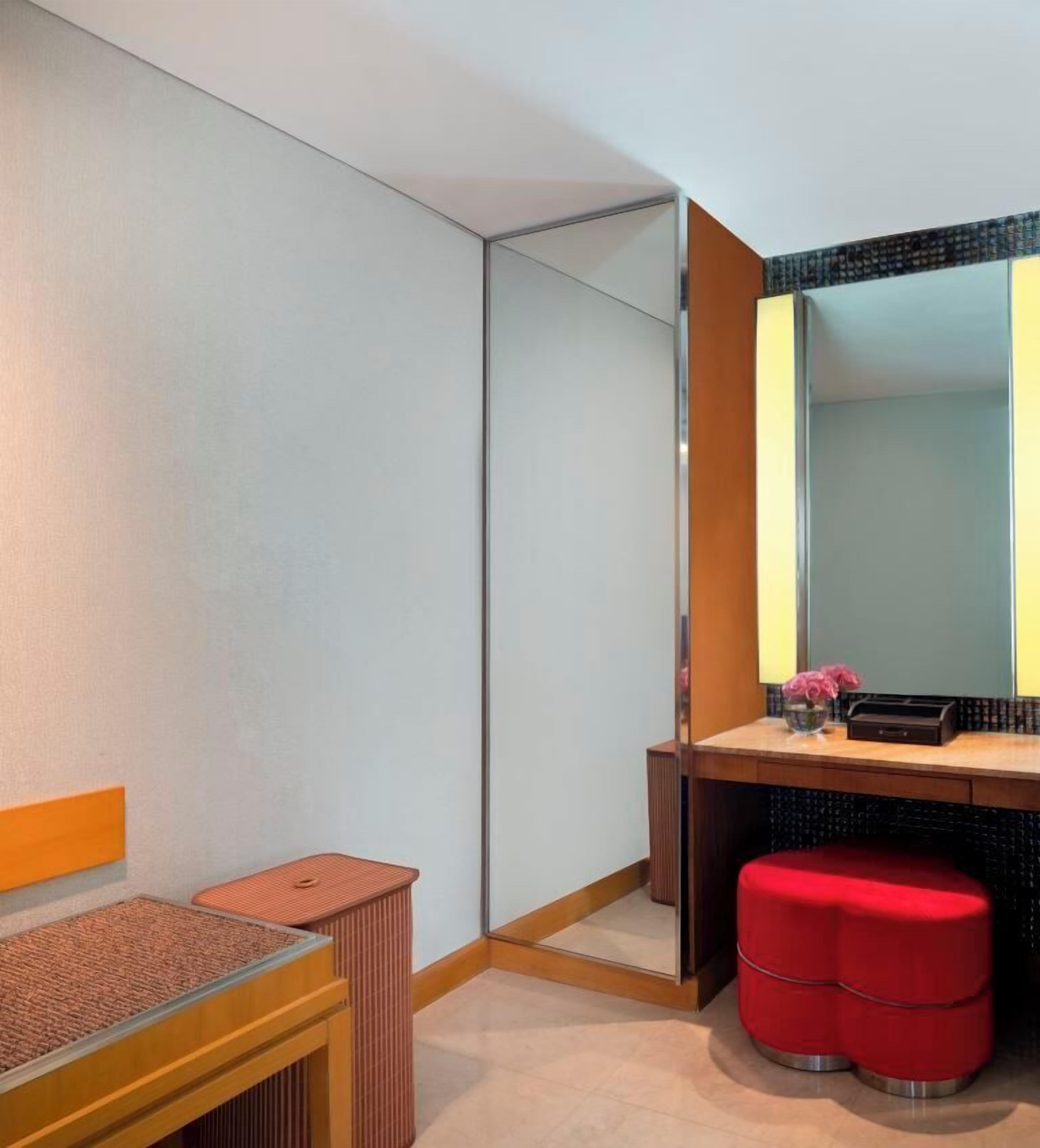 A modern bathroom with a glass partition, a wooden vanity, a red stool, and a mirror with a black frame.