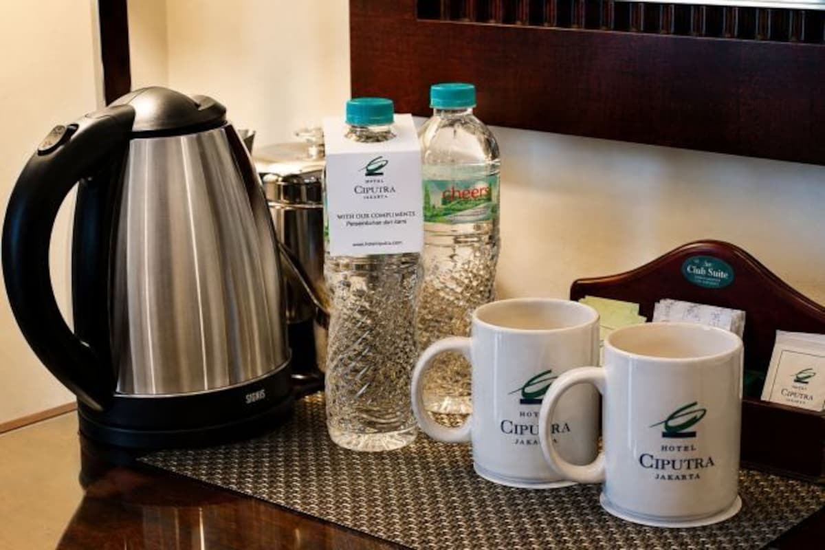 A coffee station with a kettle, Cheer water bottles, and two coffee mugs on a mat.