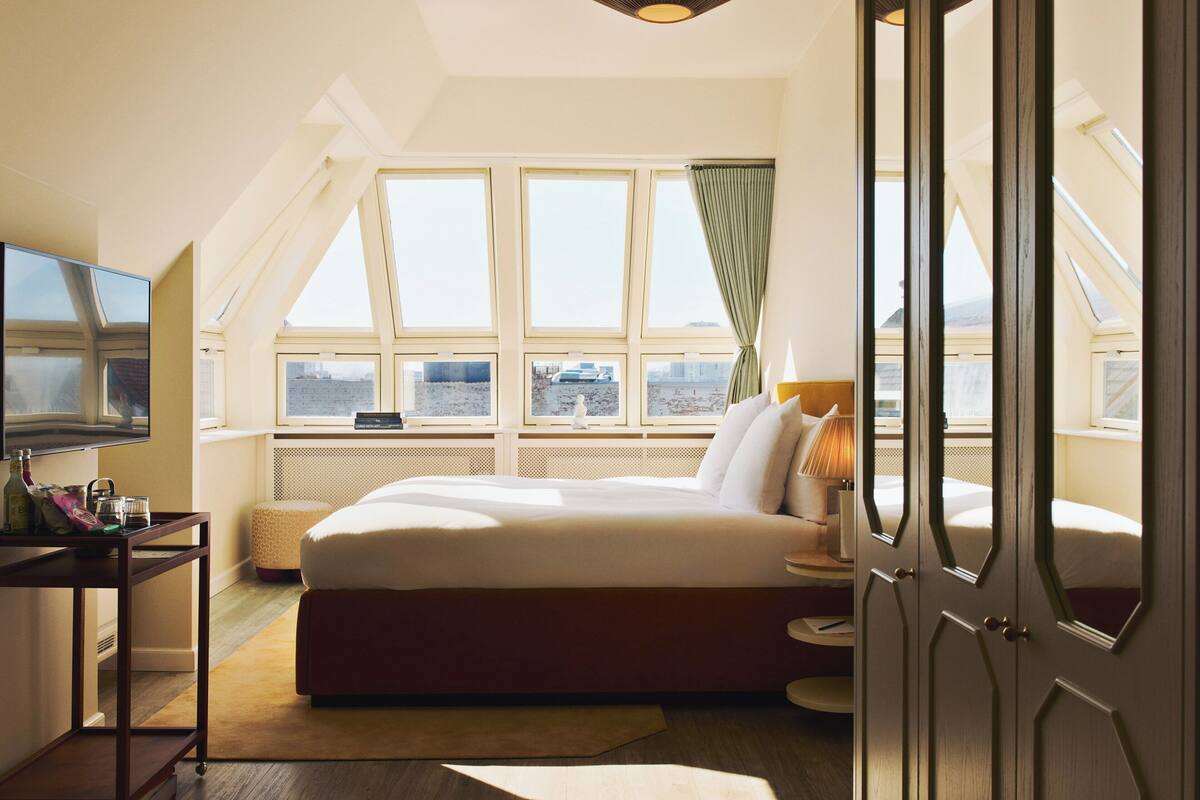 A bedroom with a large bed, a TV, a desk, and a view of the city through skylights.