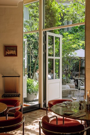 A dining area with a glass table, red chairs, and a view of the garden through a glass door.. Coco Hotel