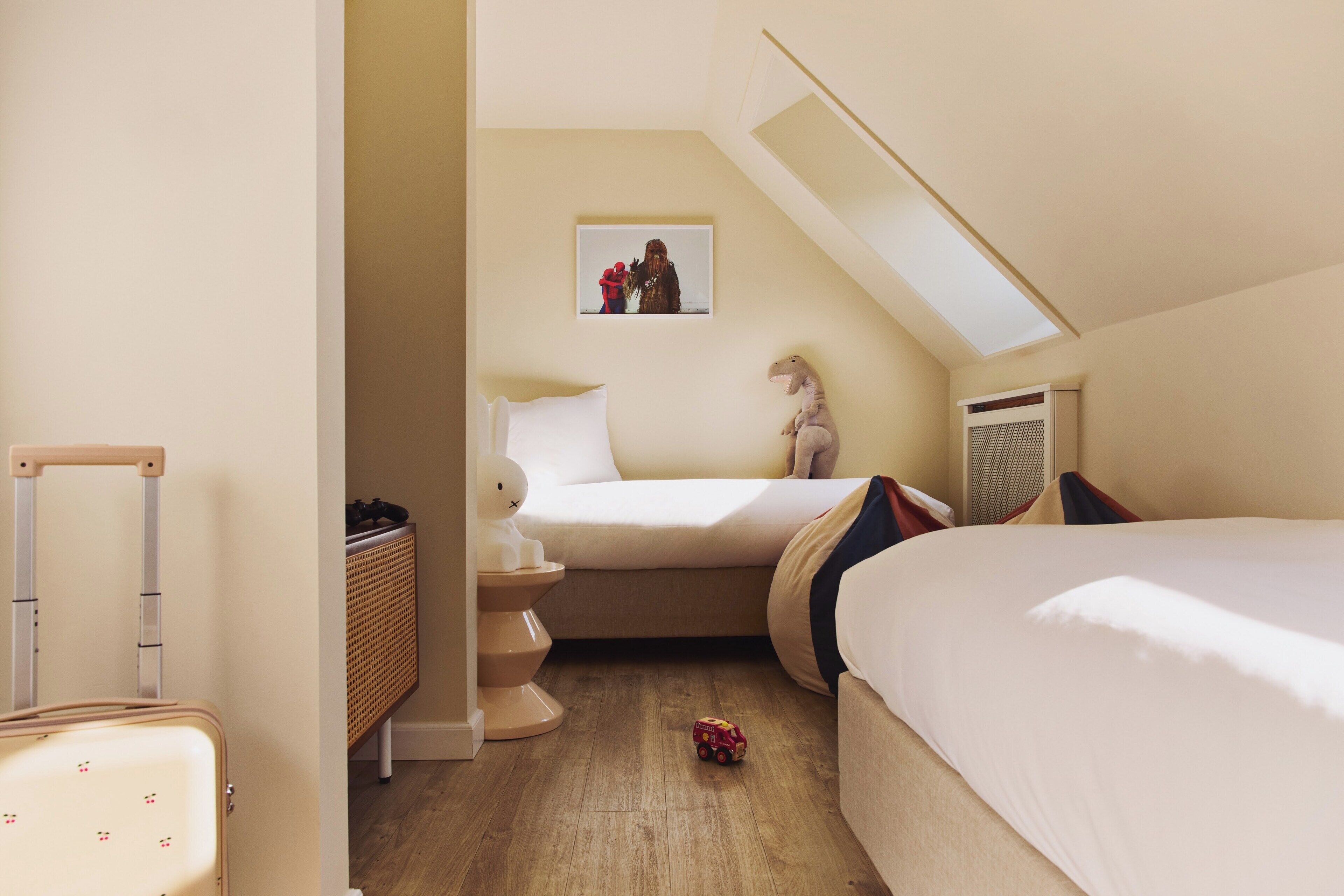 A bedroom with a bed, a bedside table, a lamp, a small dinosaur toy, and a suitcase.