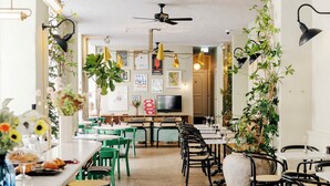 A restaurant with a central dining area, green chairs, a bar area, and hanging plants. - Coco Hotel (Copenhagen)