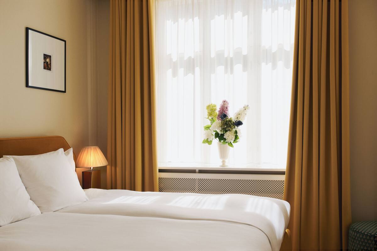 A hotel room with a bed, a picture on the wall, a lamp, and a window with curtains.