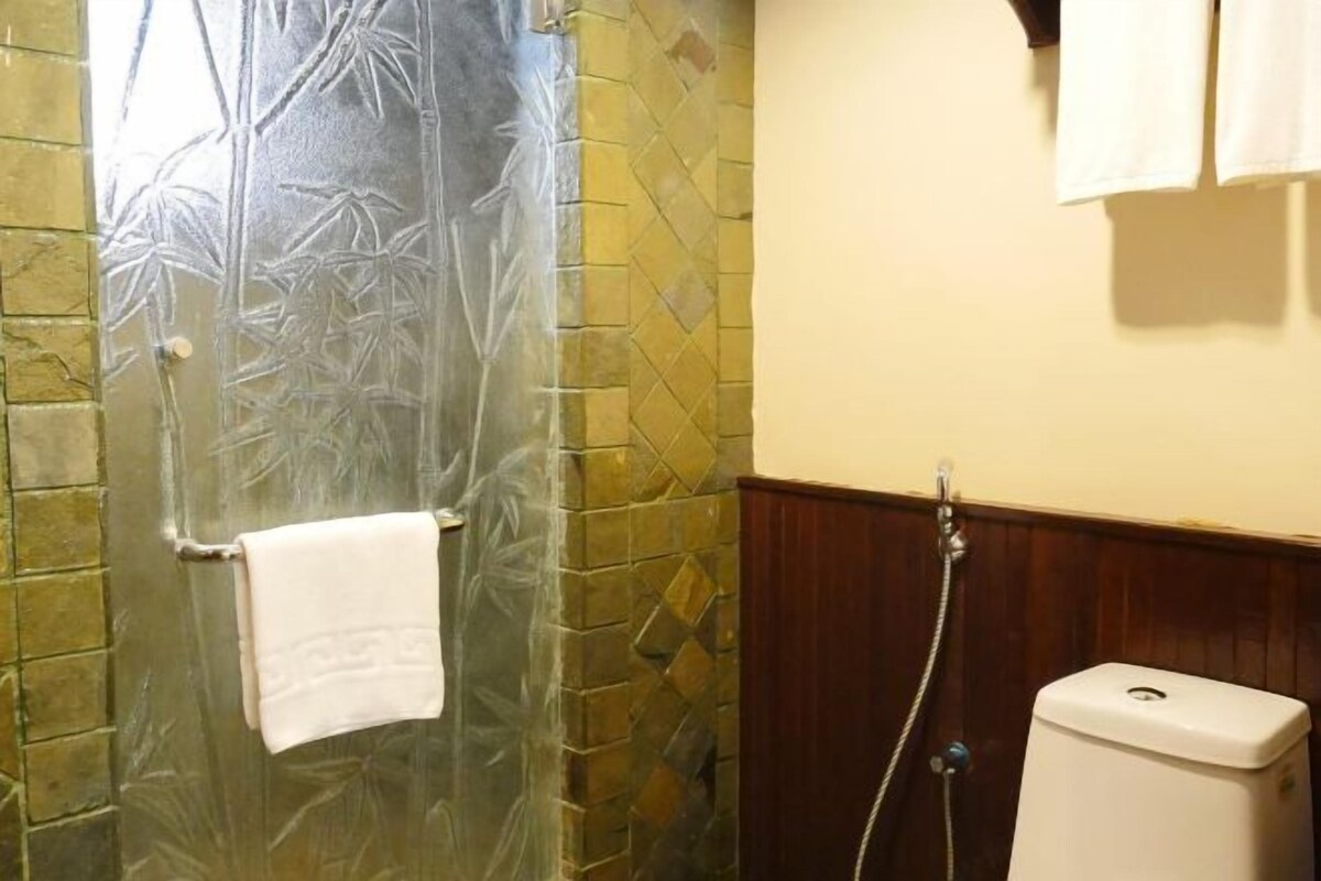 Un baño con mampara de vidrio, una toalla blanca colgada en la puerta, un inodoro y un revestimiento de pared de madera.