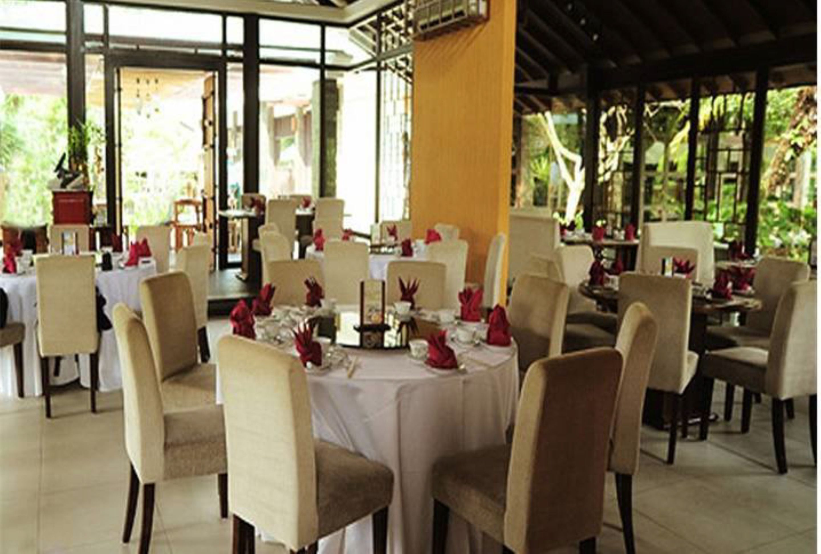 Comedor con mesas redondas dispuestas para varios comensales, sillas color beige y manteles blancos.