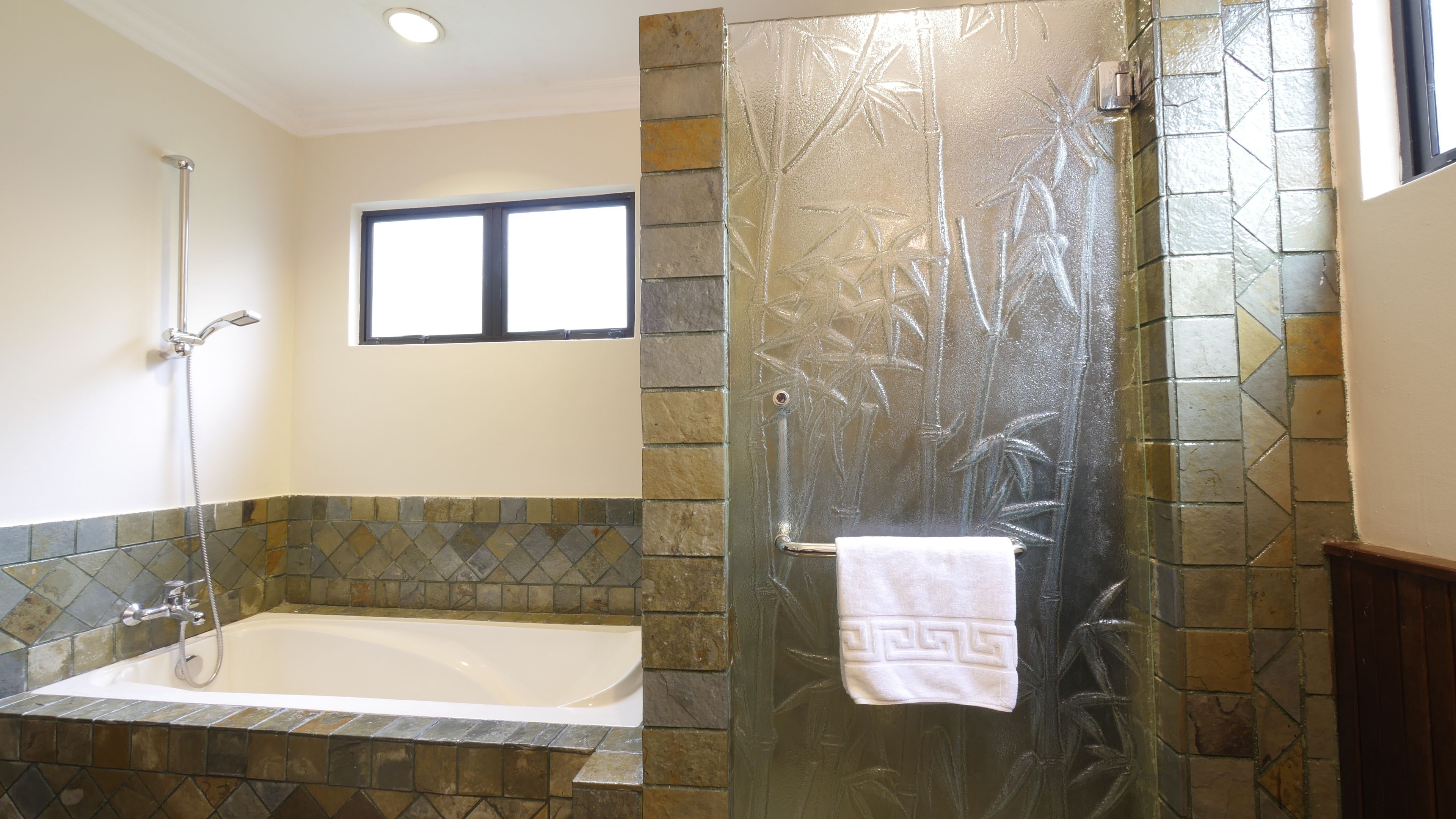 Un baño con bañera, cabina de ducha de vidrio y una ventana sobre la bañera.