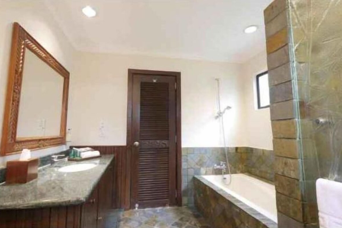 Un baño con lavamanos de mármol, puerta de madera, ducha y espejo.