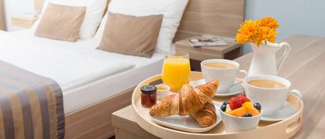 A neatly made breakfast tray with croissants, fruit, coffee, and juice on a hotel room table.