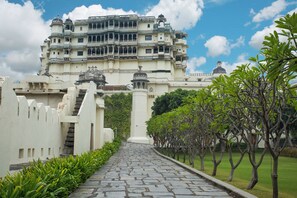 A grand building with multiple balconies and domes, a paved pathway, and well-maintained greenery.